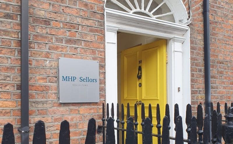 The open yellow door and fanlight entrance to MHP Sellors' office on Bindon Street in Ennis, with the firm's plaque on the brick wall